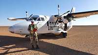 Ein Soldat steht mit Schutzhelm und Warnweste vor einem kleinen Transportflugzeug der Vereinten Nationen