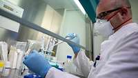 Ein Laborwissenschaftler mit Mundschutz hält eine Pipette und ein Reagenzglas 