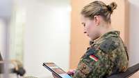 Eine Soldatin sitzt mit einem Tablet in der Hand in einer Stube der Bundeswehr