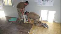 Zwei Soldaten entfernen einen alten Fußbodenbelag in einem Container