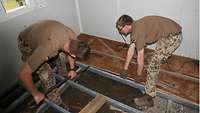 Zwei Soldaten demontieren die Holzkonstruktion des Fußbodens in einem Bürocontainer