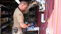 Ein Soldat prüft mit einem Messgerät die elektrischen Installationen in einem Lagercontainer