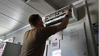 Ein Soldat reinigt und überprüft eine Klimaanlage in einem Bürocontainer