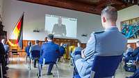 Die Lehrgangsteilnehmenden sitzen in der Aula und hören dem Stellvertreter des Inspekteurs der Marine per Videokonferenz zu.
