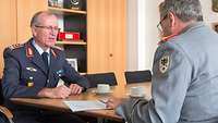 Zwei Soldaten sitzen sich an einem Tisch gegenüber, auf dem ein Blatt liegt.