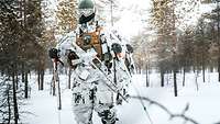 Soldaten laufen in weißer Tarnkleidung durch einen verschneiten Wald.
