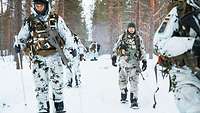 Sechs Soldaten laufen in Schützenreihe mit Schneetrittlingen in Schneetarnuniform.