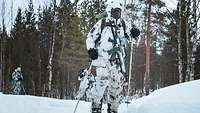 Drei Soldaten laufen in Reihe mit Skiern, Stöcken und Gewehren in Schneetarn durch einen Wald.