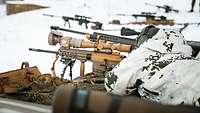 Ein Scharfschütze in Schneetarnuniform liegt mit seinem Gewehr auf dem Schnee im Anschlag.