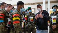 Eine Gruppe von Soldaten mit Mundschutzmasken hört einem Mann zu, der ein Smartphone in der Hand hält