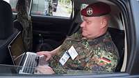 Ein Soldat sitzt in einem Auto und hat einen Laptop auf dem Schoß.