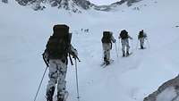 Vier Soldaten laufen in tiefem Schnee auf Skiern mit Marschgepäck hintereinander.