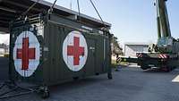 Ein Container mit einem roten Kreuz darauf hängt an einem Kran