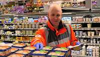 Ein Mann in einer orangefarbenen Jacke greift in einem Supermarkt nach einer Packung.