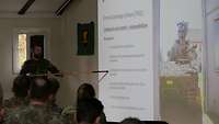Ein Soldat hält eine Präsentation und weist mit einem Zeigestock auf eine bestimmte Information