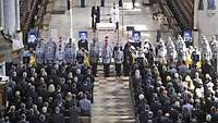 Viele Menschen stehen in einer Kirche vor vier Fotos und vier Särgen, an denen Soldaten die Wache stehen