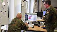 Ein Soldat sitzt in einem Raum am Rechner, einer steht daneben.