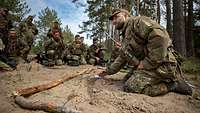 Ein Soldat kniet im Wald und erklärt am Boden Besonderheiten der kommenden Operation.