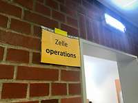 Ein gelbes Schild mit der Aufschrift "Zelle Operations" an einer Backsteinwand, daneben eine offene Tür.