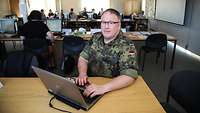 Ein Soldat arbeitet in einem großen Besprechungsraum an seinem Laptop.