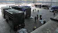 Blick auf die Lastkraftwagen des Sanitätsdienstes der Bundeswehr und Fahrzeuge des THW Gütersloh in einer großen Lagerhalle.