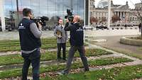 Ein Soldat im Dienstanzug steht vor zwei Kameramännern, dahinter ein Gebäude.