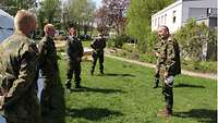 Mehrere Soldaten im Gespäch mit einem General auf einer Wiese.