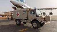 Der gelieferte Krankenwagen steht auf dem Flughafen. Im Hintergrund steht die Iljuschun IL-76