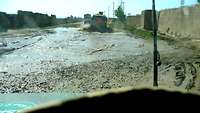 Blick aus einem Fahrzeug: Pfützen, Kies und Schlamm auf unbefestigter Straße