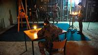 Ein Soldat sitzt an einem Tisch und trägt sich im Kerzenschein in ein Buch ein.