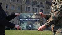 Die Arme jeweils eines zivilen und militärischen Beschäftigten halten ein Banner mit dem Slogan "Für euch gemeinsam stark".