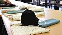 Eine fertige schwarze Mundschutzmaske liegt auf dem Tisch in der Werkstatt auf Stoffbahnen.