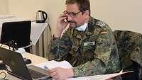 Ein Soldat in Uniform sitz vor seinem Laptop und telefoniert mit dem Handy.