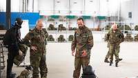Zwei Soldaten unterhalten sich in einer großen Halle, im Hintergrund in Regalen Sprungausrüstungen.