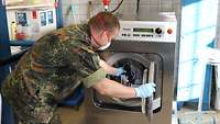 Ein Soldat mit Handschuhen und Mundschutz legt neue Masken in eine Industriewaschmaschine.