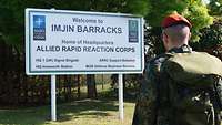 Ein Soldat steht vor einem großen, weißen Schild, dahinter Bäume und Sträucher.