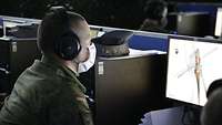 Ein Soldat sitzt mit einer Schutzmaske vor einem hell erleuchteten Computerbildschirm.