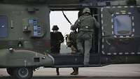 Drei Soldaten mit Mund-Nasenschutz steigen in einen Hubschrauber ein.
