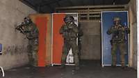 Drei Soldaten stehen mit Gewehr im Anschlag in einem Raum. Sie tragen Helme und ABC-Schutzmasken.