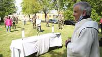 Ein Pfarrer steht am Altar, vor ihm verteilt Soldaten und zivile Mitarbeiter auf einer Wiese.