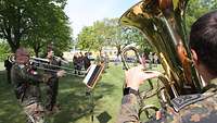 Soldaten mit Trompete, Posaune und Tuba stehen auf einer Wiese und machen Musik.