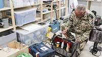 Ein Soldat kniet in einem Materiallager und packt einen Schraubenzieher in eine Werkzeugtasche