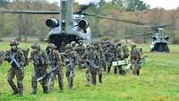 Zwei Hubschrauber stehen auf einer Wiese. Bewaffnete Soldaten verlassen nacheinander die Flieger.