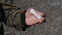 Ein Soldat hält ein rund fünf Zentimeter langes, beschriftetes Röhrchen in der Hand.