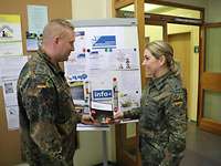 Ein weiblicher Soldat übergibt mit einem Lächel eine Informations Broschüre an einen anderen Soldaten.