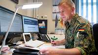 Ein Soldat sitzt an seinem Schreibtisch zwei Bildschirmen und einem Laptop.