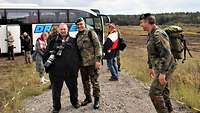 Zwei Soldaten stehen vor einem weißen Bus, um sie herum Journalisten mit und ohne Kameras.