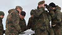 Soldaten im Feldanzug stehen in einer Gruppe zusammen und halten eine Landkarte, einer Blick durch ein Fernglas.