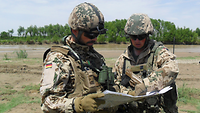 Ein Soldat mit Helm und Schutzbrille hält eine Karte, ein anderer zeigt etwas auf der Karte.