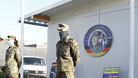 Drei Soldaten stehen mit Gesichtsschutz und einigem Abstand zueinander vor einem Gebäude
